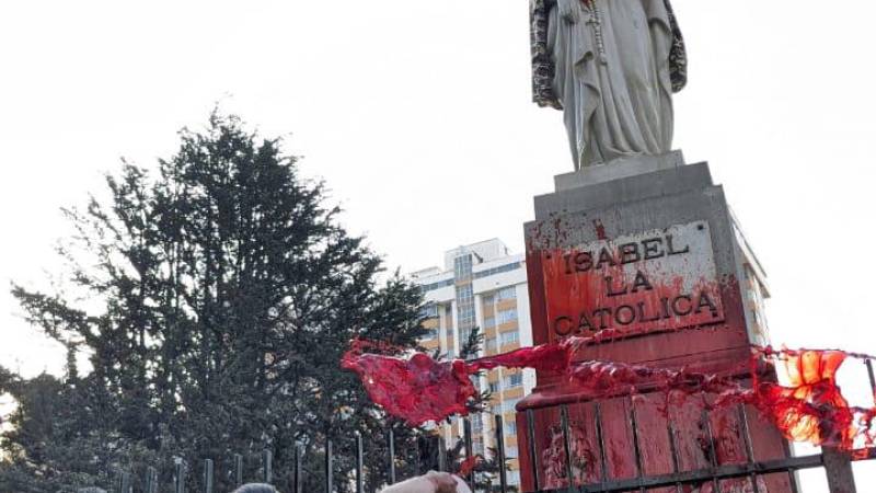 Una mujer de pollera echa pintura roja a la estatua