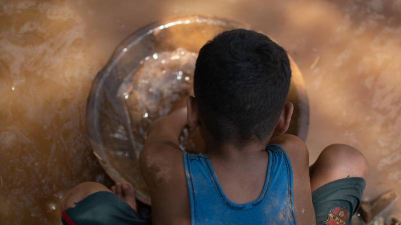 Un niño minero venezolano descarga una bolsa de barro en un recipiente.