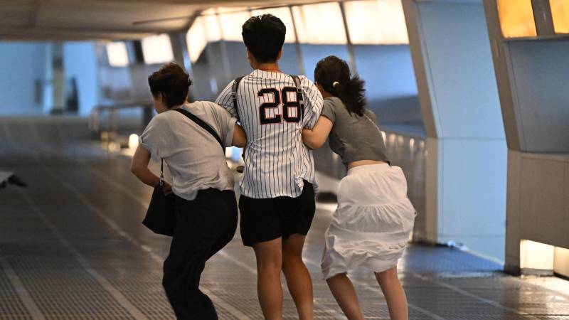 People brace themselves against strong winds in Central district with typhoon signal number 10 hoisted as Typhoon Wipha moves within 60km of Hong Kong on July 20, 2025. (Photo by Peter PARKS / AFP)