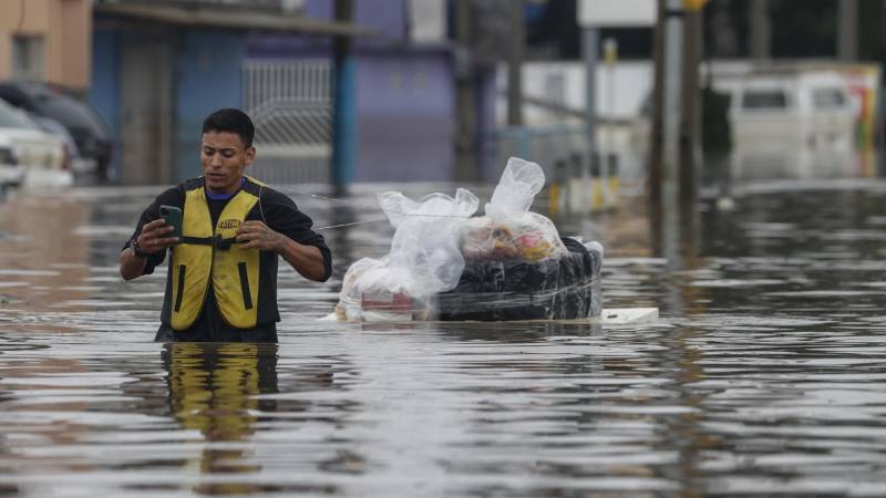 Un hombre transporta suministros en una tabla en medio de una calle inundada.