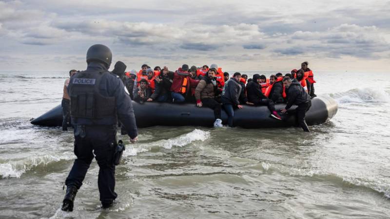 Los migrantes reaccionan mientras un policía francés se prepara para perforar el barco de un traficante.